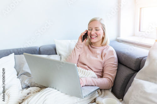 Happy cheerful young woman talking on the phone at home, smiling teen girl making answering call by cellphone sitting on sofa, beautiful lady having pleasant funny conversation speaking by mobile