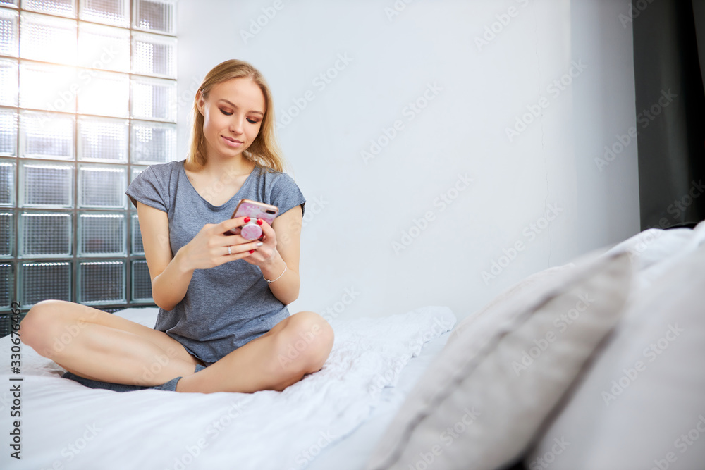 young caucasian good-looking lady chatting with friend while she is on bed at home. attractive woman look at smartphone and smile. after waking up in morning young caucasian good-looking lady chatting with friend while she is on bed at home. attractive woman look at smartphone and smile. after waking up in morning