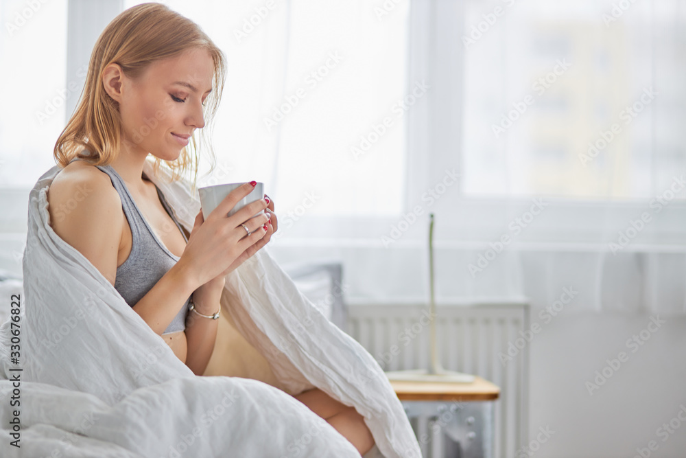 beautiful caucasian lady sit drinking hot tea or coffee on bed at home, in morning. blond female in underwear just woke up beautiful caucasian lady sit drinking hot tea or coffee on bed at home, in morning. blond female in underwear just woke up
