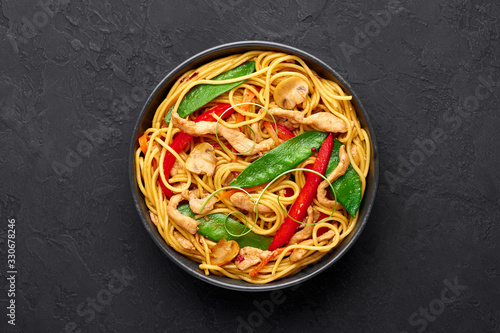 Chicken Lo Mein in black bowl at dark slate background. Lo Mein is Chinese cuisine dish with chicken meat, egg noodles, vegetables and sauces. Chinese Food. Stir Fried Noodles. Copy space. Top view photo