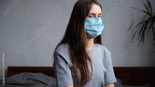 Young woman sit on bed protects face with mask, thinks abot risk of epidemic disease, girl having health problem flue hay fever alone in bedroom. Concept safety, N1H1 coronavirus, virus protection photo