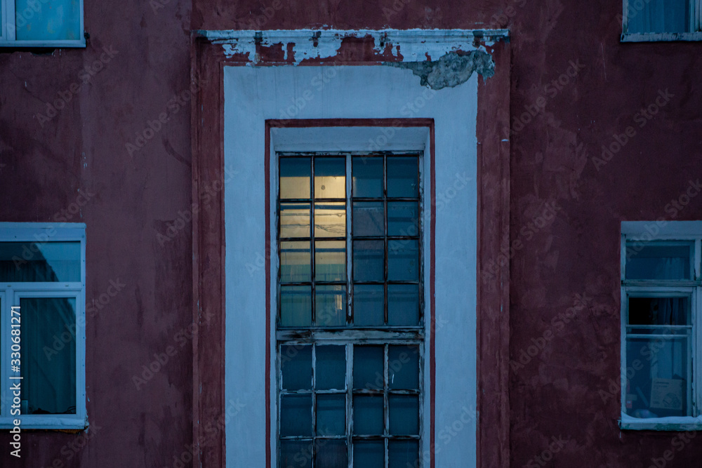 House windows and glass entrance on the red concrete wall covered with snow