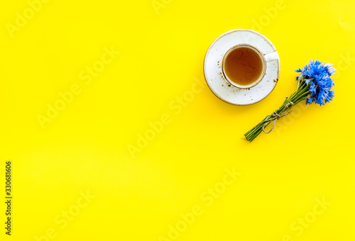 Summer tea party. Cup near cornflowers bouquet on yellow background top-down copy space