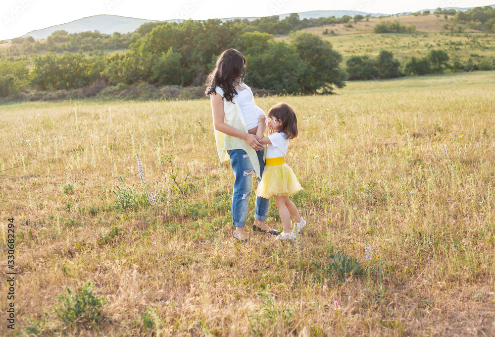 Active female child runs to the pregnant motheк and hugging on the meadow Active female child runs to the pregnant motheк and hugging on the meadow