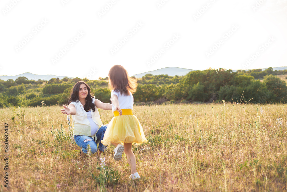 Fototapeta premium Active female child runs to the pregnant motheк on the meadow