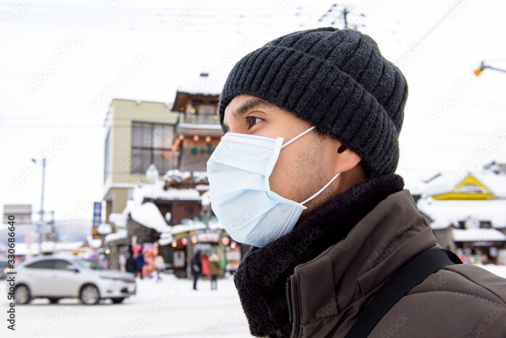 Asian tourist man wearing mask protecting from Coronavirus while walking outdoors during winter in Hokkaido Japan Asian tourist man wearing mask protecting from Coronavirus while walking outdoors during winter in Hokkaido Japan
