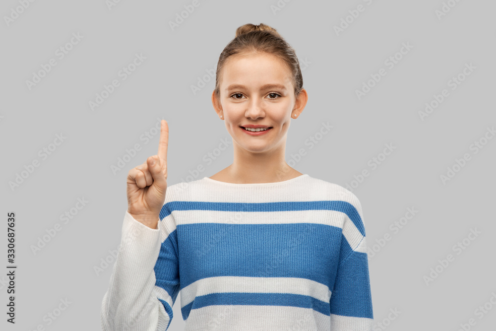 gesture, count and people concept - smiling teenage girl in pullover pointing one finger up over grey background gesture, count and people concept - smiling teenage girl in pullover pointing one finger up over grey background