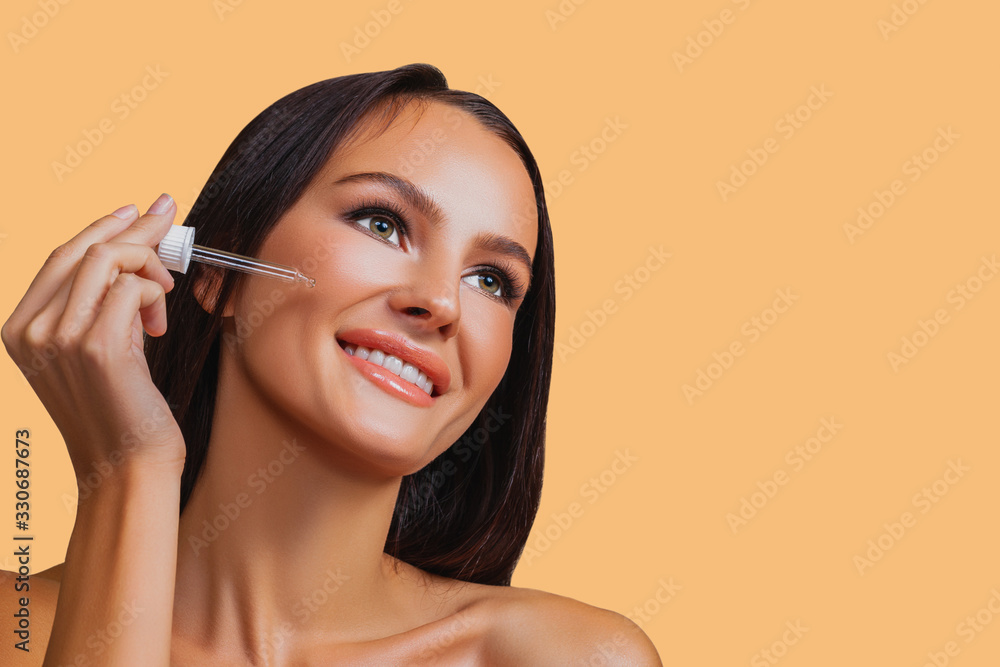 Beauty girl applying serum on face with pipette. Happy beautiful girl with perfect clean healthy skin looking to the side. Pretty woman clean fresh skin. Expressive facial expressions. Cosmetology. 