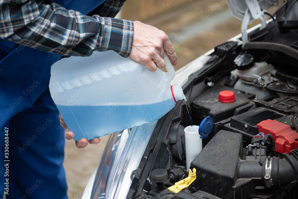Hands of mechanic pouring windshield washer fluid in a car Hands of mechanic pouring windshield washer fluid in a car