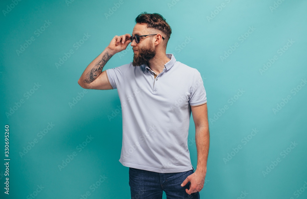 Handsome hipster guy with beard wearing blue polo t-shirt with space for your brand name or label. Mockup for print. - obrazy, fototapety, plakaty 