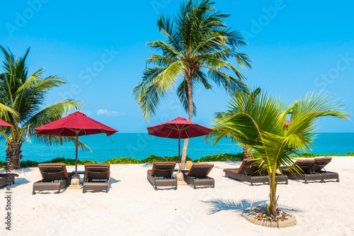 Beautiful tropical beach sea ocean with umbrella and chair around coconut palm tree on blue sky © siraphol