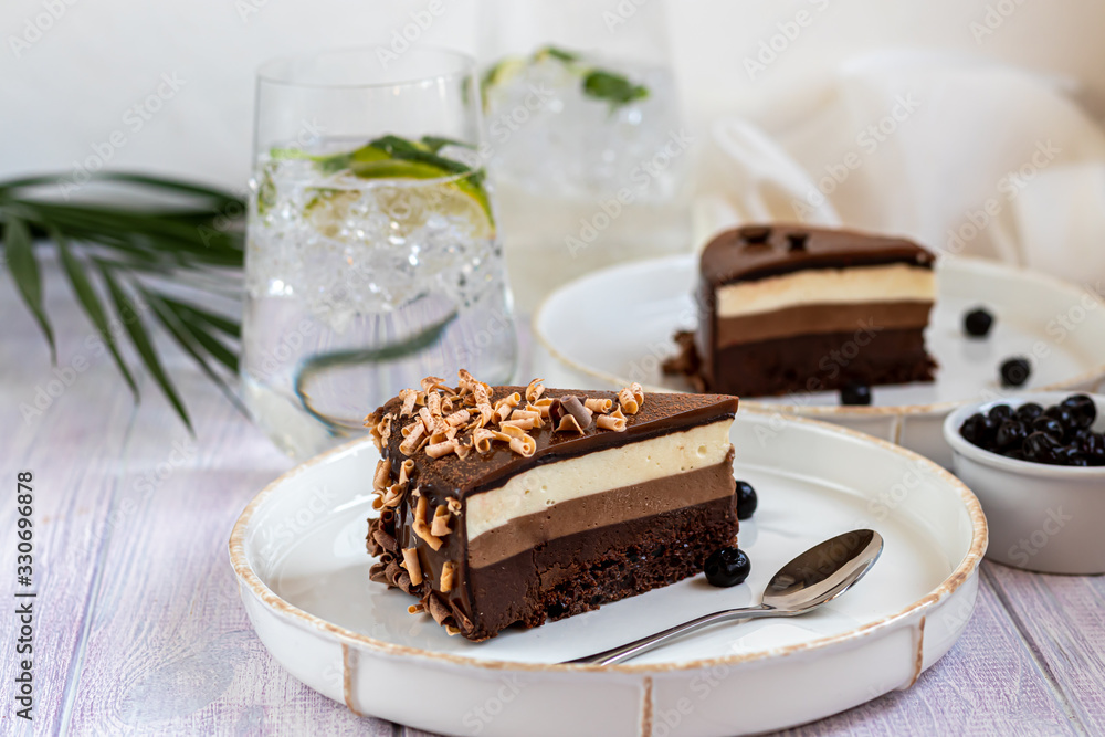 Holiday cake Three chocolates. Two white plates have two servings. On a light background. Birthday, holidays, sweets. Holiday cake Three chocolates. Two white plates have two servings. On a light background. Birthday, holidays, sweets.