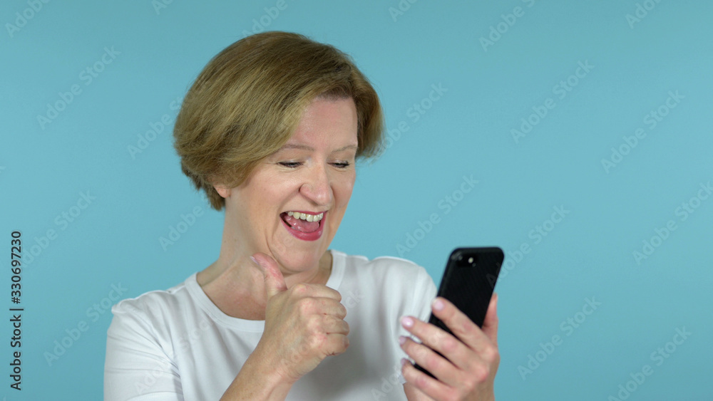 The Old Woman Excited for Success while Using Smartphone Isolated on Blue Background The Old Woman Excited for Success while Using Smartphone Isolated on Blue Background