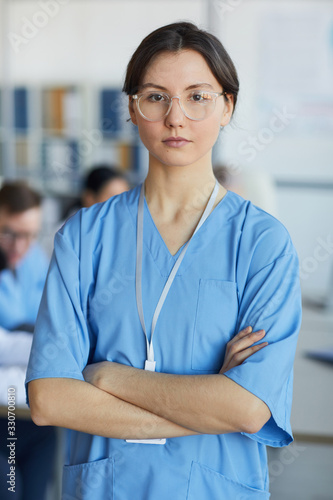 Waist up portrait of young nurse wearing glasses standing with arms crossed and looking at camera against medical conference background