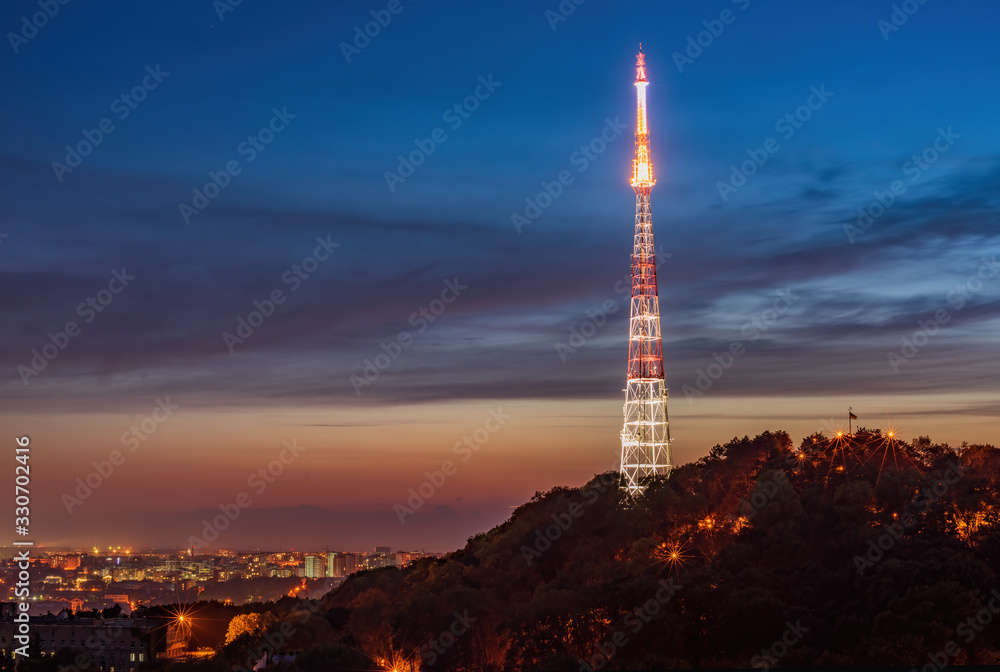 Amazing panoramic view of High Castle hill with illuminated TV tower against picturesque sunset sky, Lviv, Ukraine.