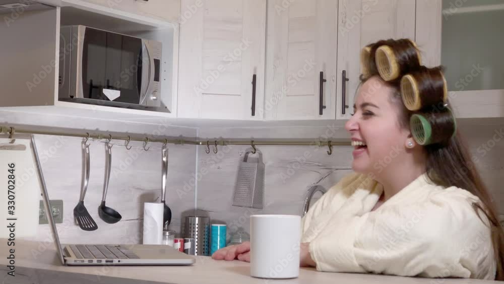 Plus-size girl, dressed in a bathrobe, curlers on her head, talking by video call Plus-size girl, dressed in a bathrobe, curlers on her head, talking by video call