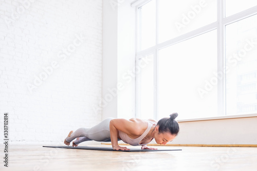 Hardy young caucasian woman in a tracksuit does limbed staff exercise chaturanga dandasana on floor during training at home. Concept of recovery after childbirth and losing weight at home. Copyspace