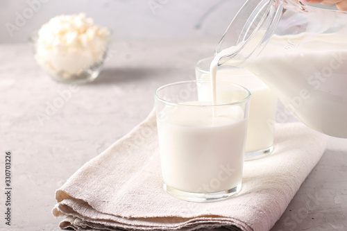 Kefir or Ayran fermented drink is poured into a glass from a jug, as well as cottage cheese in a bowl on a light gray background, Copy space photo