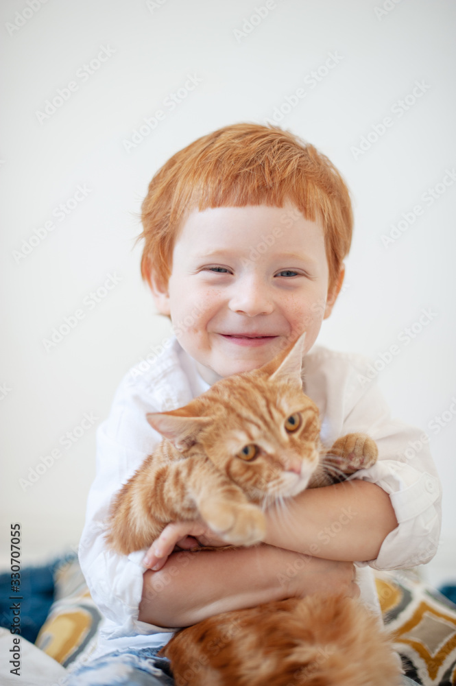 Funny red-haired boy in white bed with a red cat Funny red-haired boy in white bed with a red cat