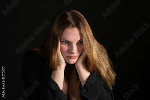 Sad teen girl on a black background with head in hands.