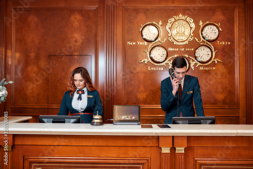 Working process. Attractive executives at the reception desk of a hotel. Young man answering phone call