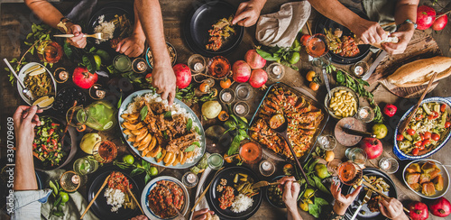 Flat-lay of family feasting with Turkish cuisine lamb chops, quince, bean, vegetable salad, babaganush, rice pilav, pumpkin dessert, lemonade over rustic table, top view, wide composition