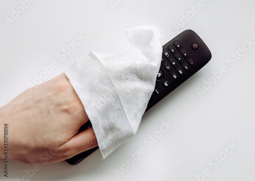 Close up view of man hand using antibacterial wet wipe for disinfecting home TV remote control.