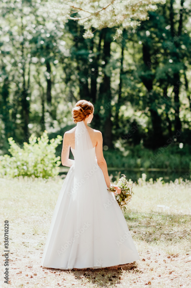 the bride in a white dress stands with her back to us and holds a bouquet of flowers