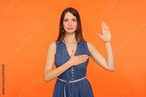 Fotografia I swear! Dedicated honest brunette woman in denim dress standing with promise hand sign, gesturing palm up, giving promise, pledging allegiance