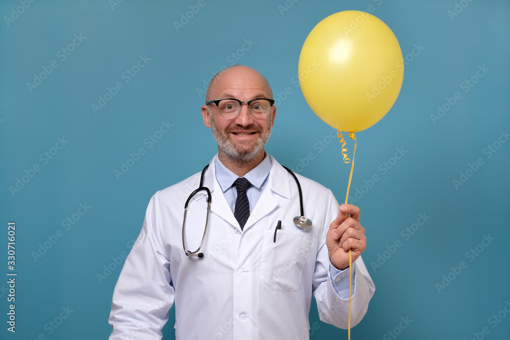 Caucasian mature man doctor surgeon with balloon having a happy birthday mood. Studio shot on blue wall Caucasian mature man doctor surgeon with balloon having a happy birthday mood. Studio shot on blue wall