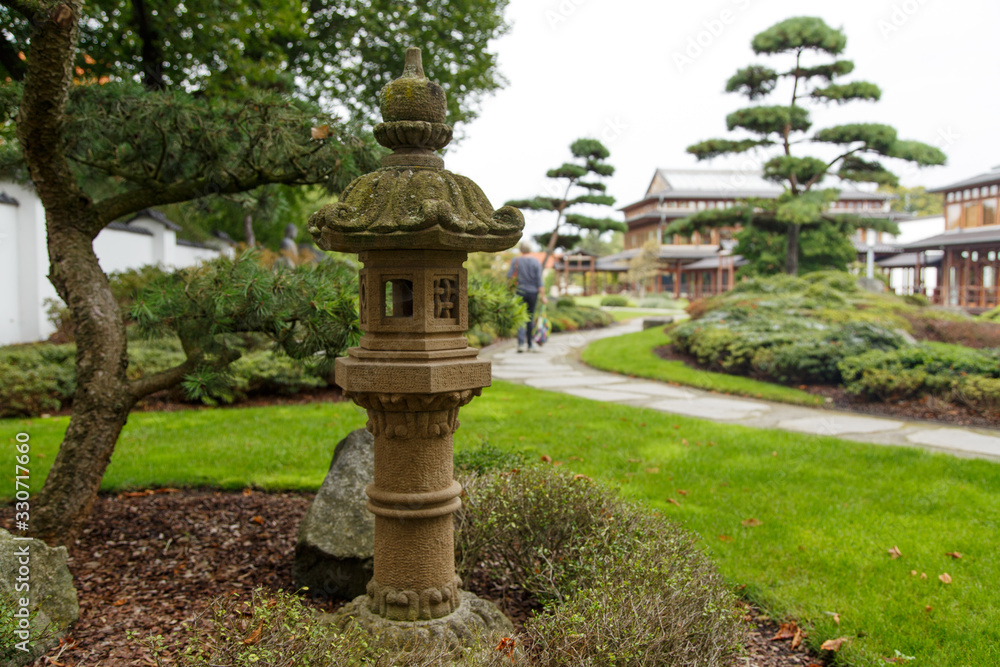 asian antique stone lantern with path on which a woman walks through park with asian topiaries and solitary shrubs asian antique stone lantern with path on which a woman walks through park with asian topiaries and solitary shrubs