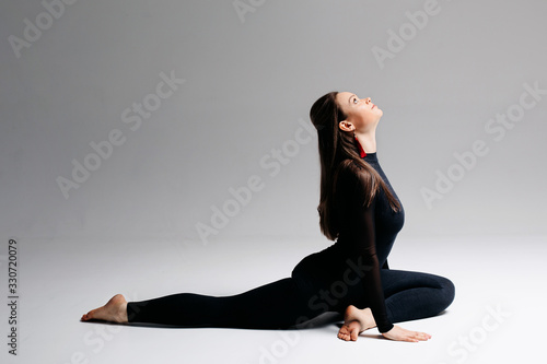 A beautiful girl of European appearance brunette sits in a difficult pose from yoga. she is looking up. Legs in twine. Photo on a white background.