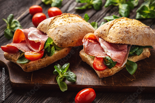 Jamon sandwiches with tomatoes, on wooden board.