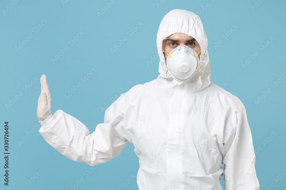 Man in white protective suit respirator mask isolated on blue background studio. Epidemic pandemic new rapidly spreading coronavirus 2019-ncov originating in Wuhan China, medicine flu virus concept. Man in white protective suit respirator mask isolated on blue background studio. Epidemic pandemic new rapidly spreading coronavirus 2019-ncov originating in Wuhan China, medicine flu virus concept.