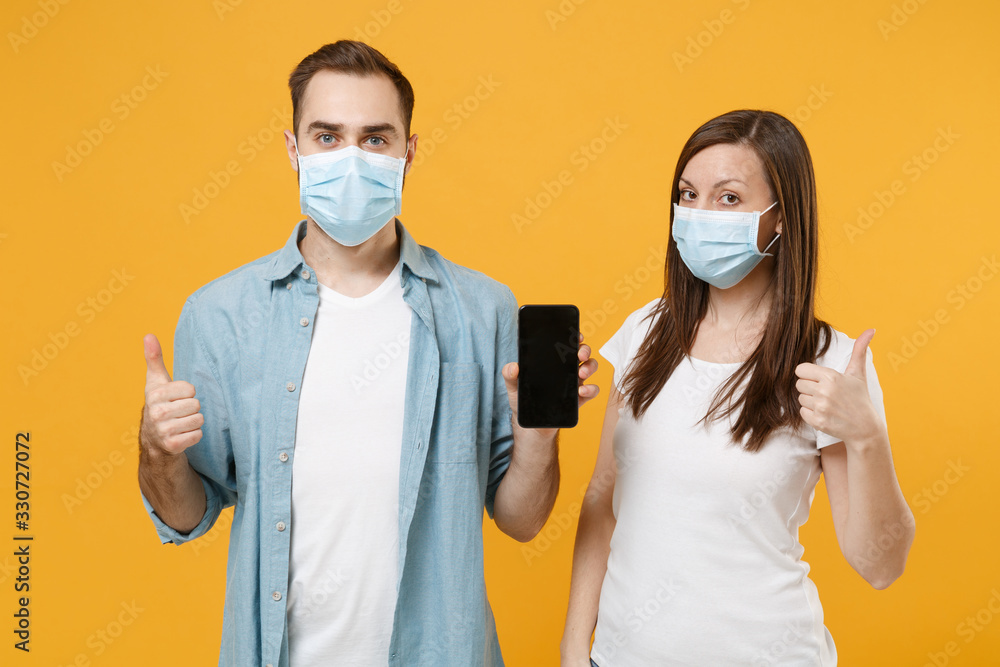 Two people in sterile face masks hold mobile phone isolated on yellow background studio. Epidemic pandemic rapidly spreading coronavirus 2019-ncov medicine flu virus ill sick disease treatment concept