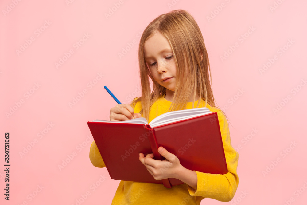 Child doing homework. Portrait of clever little girl writing poem in book with serious concentrated expression, development of creative child abilities. indoor studio shot isolated on pink background Child doing homework. Portrait of clever little girl writing poem in book with serious concentrated expression, development of creative child abilities. indoor studio shot isolated on pink background