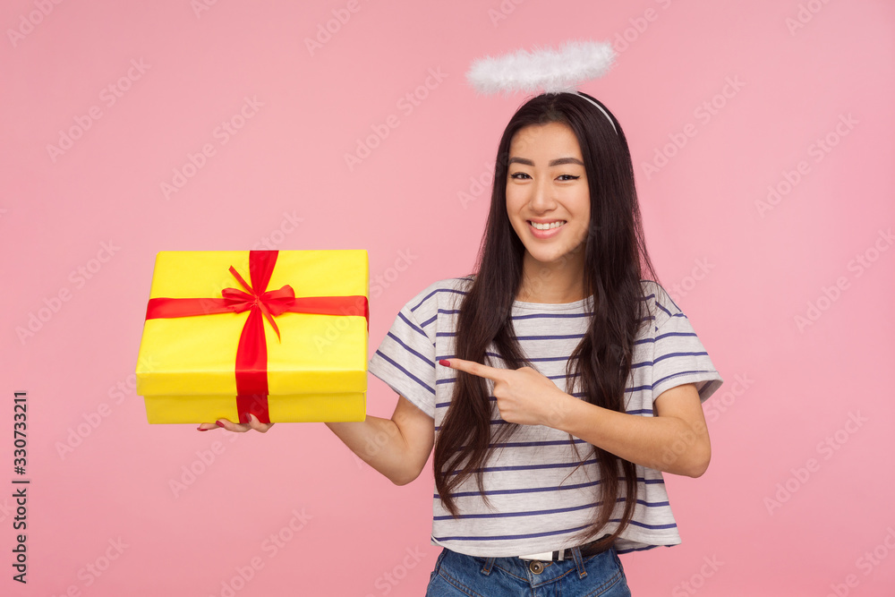 Portrait of positive angelic asian woman with halo over head smiling happily and pointing at gift box, kind generous girl offering holiday present. indoor studio shot isolated on pink background Portrait of positive angelic asian woman with halo over head smiling happily and pointing at gift box, kind generous girl offering holiday present. indoor studio shot isolated on pink background