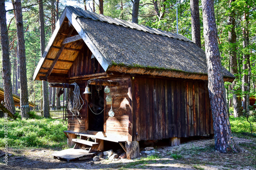 Lielupe / Jurmala, Latvia - Old fishing wooden house with a straw roof and a bell at the entrance, located in the Jurmala Maritime Museum, a forest in the summer during the daytime.