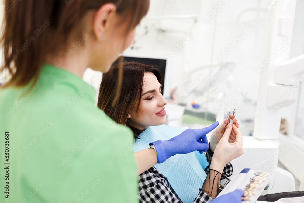 Dentist shows crown samples to his patient. Woman at the dentist's appointment chooses the tone of veneers Dentist shows crown samples to his patient. Woman at the dentist's appointment chooses the tone of veneers