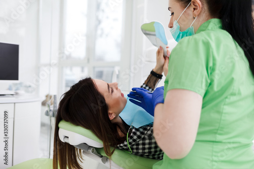 Dentist examining teeth for patient. Girl looks in the mirror at the process of checking teeth
