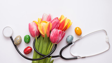 Bunch of colorful tulips, easter eggs and stethoscope on light background. Happy nurse day. Easter. Copy space.