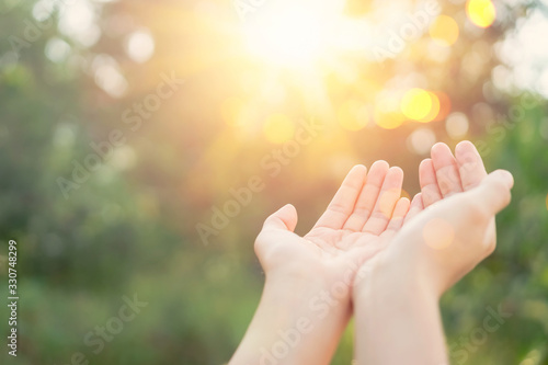 Woman open hand up to sunset sky and green blur leaf bokeh sun light abstract background. © tonktiti
