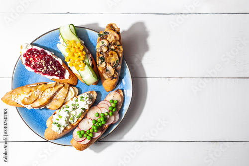 Assorted bruschetta or tapas set with different savory and sweet topping on plate and white background.Open toasts sandwich with vegetable and fruit top view flat lay copy space.Horizontal orientation