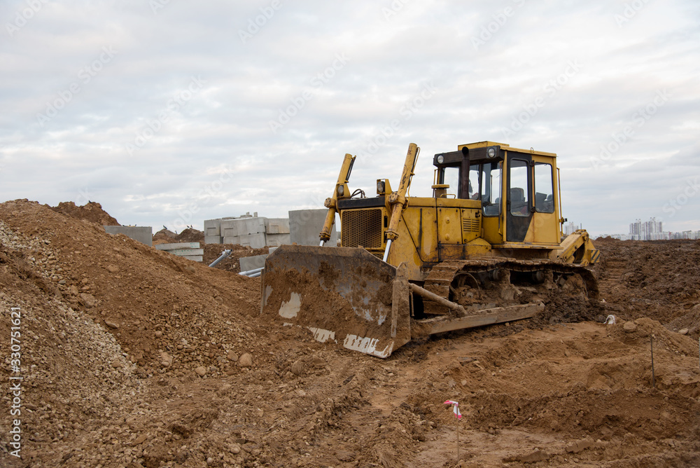 Bulldozer during land clearing and foundation digging at large construction site. Crawler tractor with bucket for pool excavation and utility trenching. Dozer, Earth-moving equipment Bulldozer during land clearing and foundation digging at large construction site. Crawler tractor with bucket for pool excavation and utility trenching. Dozer, Earth-moving equipment