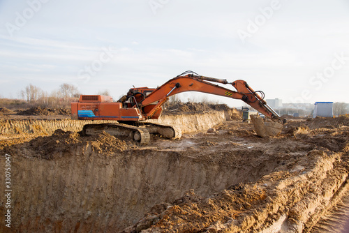 Excavator working at construction site. Backhoe digs ground for the foundation and for paving out sewer line. Construction machinery for excavating, loading, lifting and hauling of cargo on job sites photo