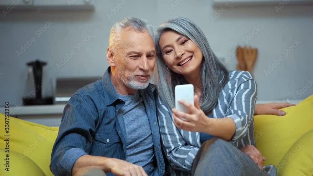 senior interracial couple waving hands and looking at smartphone senior interracial couple waving hands and looking at smartphone