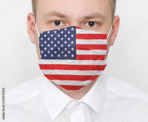 A man in a protective mask on his face with the flag of America. The concept of coronavirus and viral infections in the country, portrait, USA