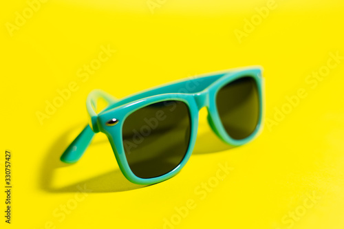 Close-up of cyan sunglasses, on background of yellow color.