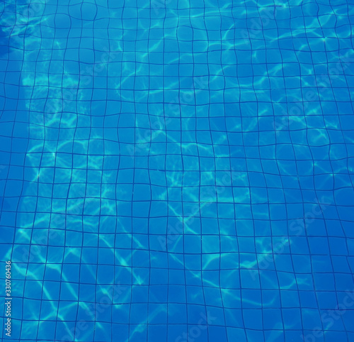 Swimming pool with the blue water and sunny reflection. Bottom swimming pool texture.