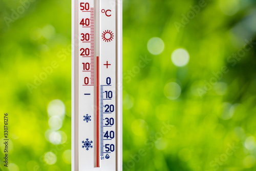 A thermometer on a blurred background of green grass shows 20 degrees of heat_ photo